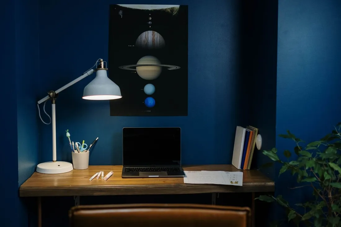 Biurko z lampką i laptopem przy granatowej ścianie z plakatem planet