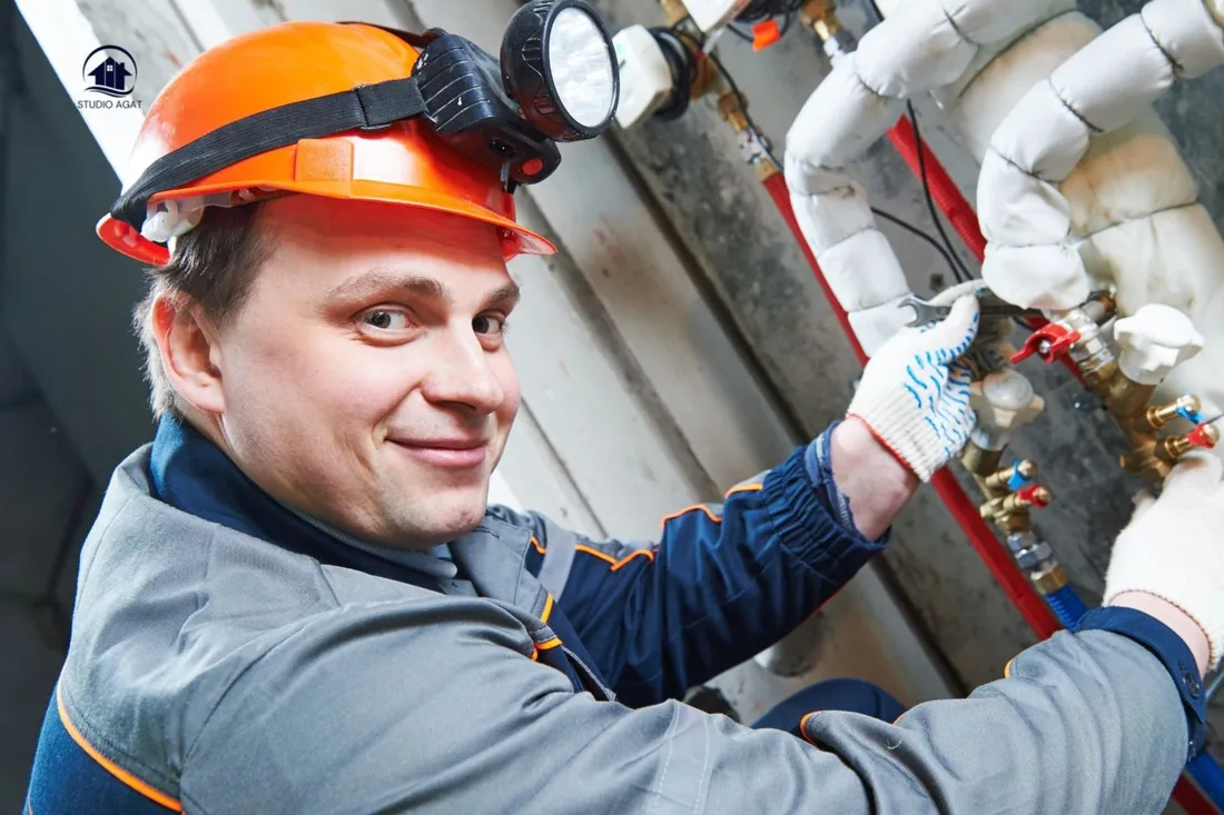 Uśmiechnięty hydraulik w kasku z latarką montuje rozdzielacz instalacji grzewczej