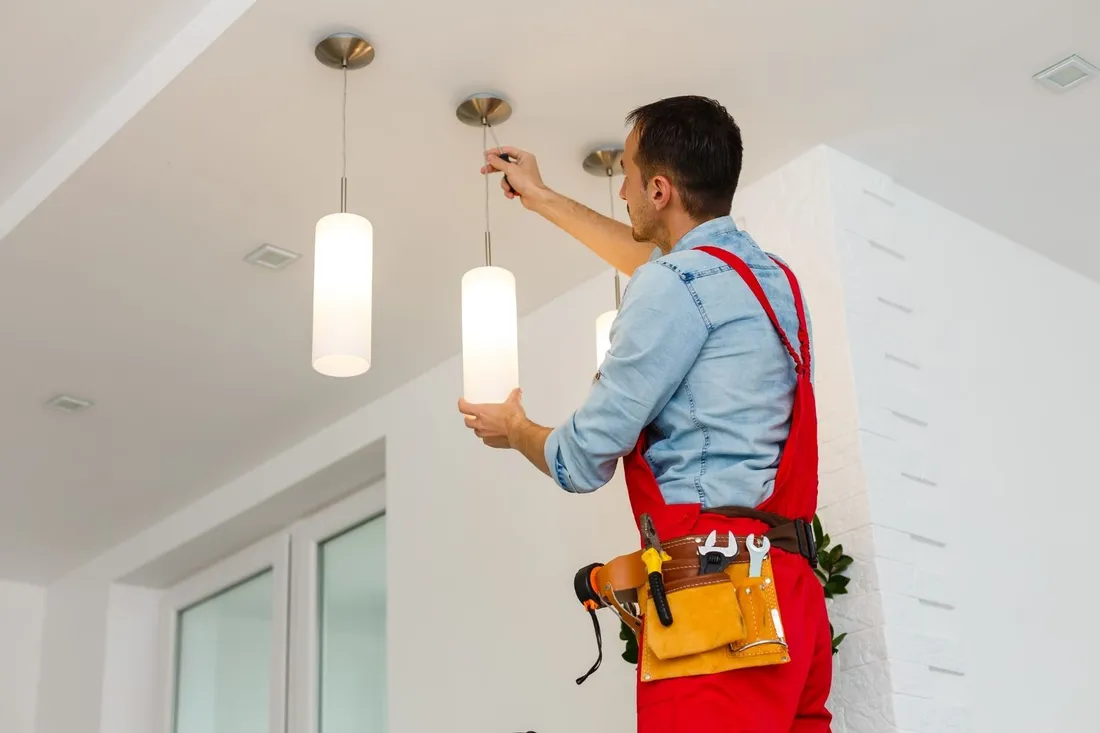 Elektryk w czerwonych ogrodniczkach montuje lampy wiszące pod sufitem