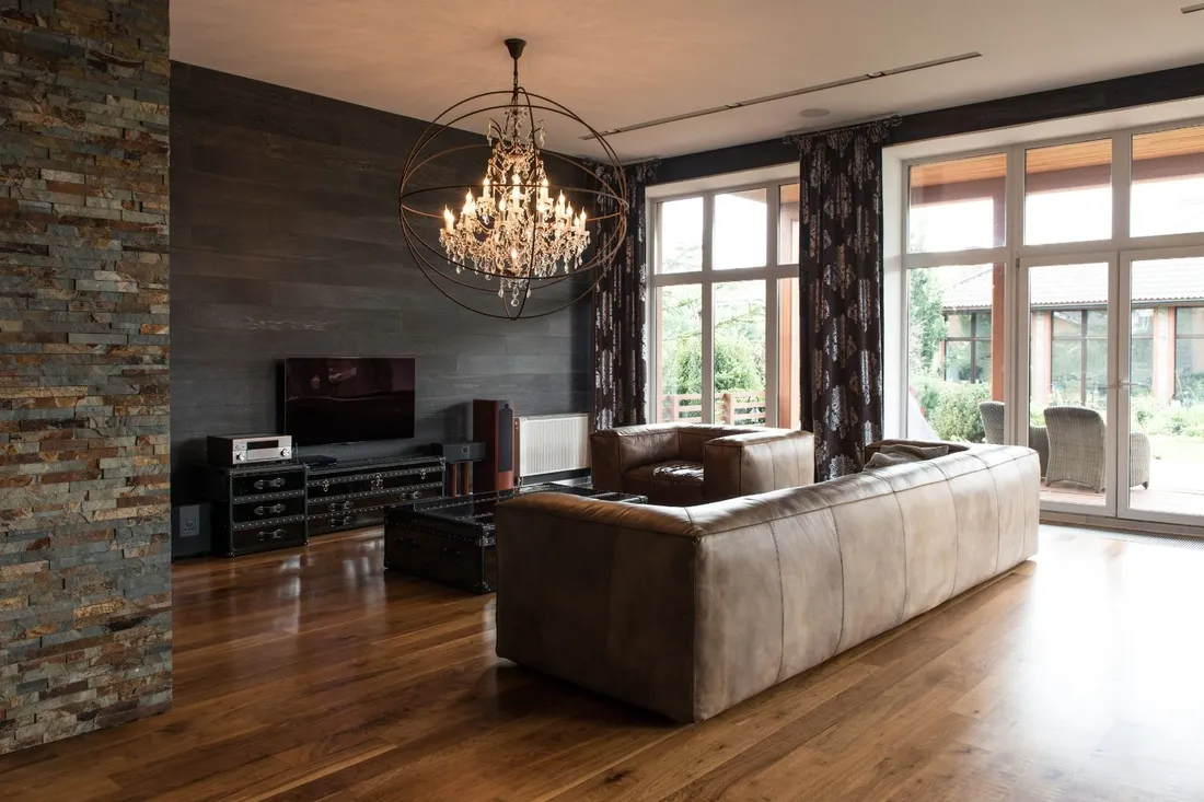 Salon z kamienną kolumną, brązową skórzaną sofą i kryształowym żyrandolem